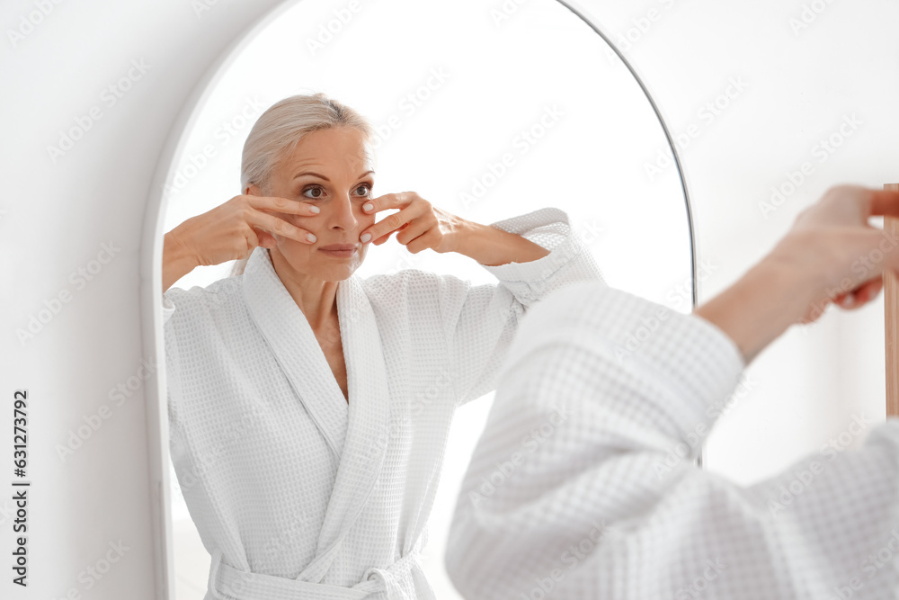 Mature woman doing face building exercise near mirror in bathroom