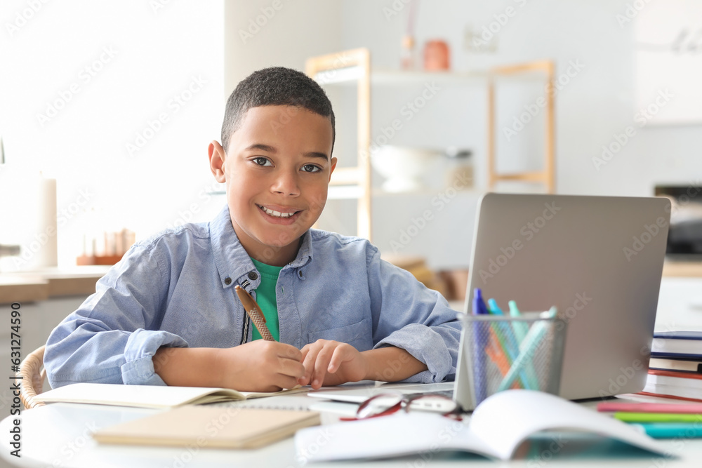 Little African-American boy studying computer sciences online in kitchen