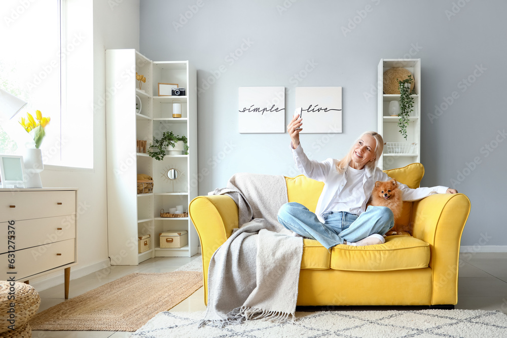 Mature woman with Pomeranian dog taking selfie at home