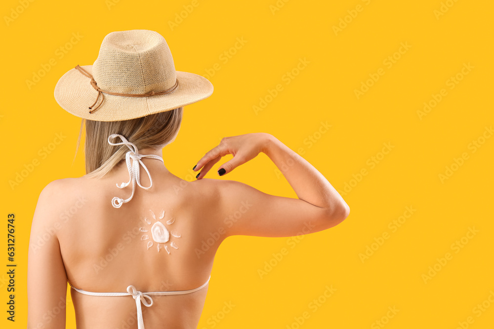 Young woman with sun made of sunscreen cream on her back against yellow background