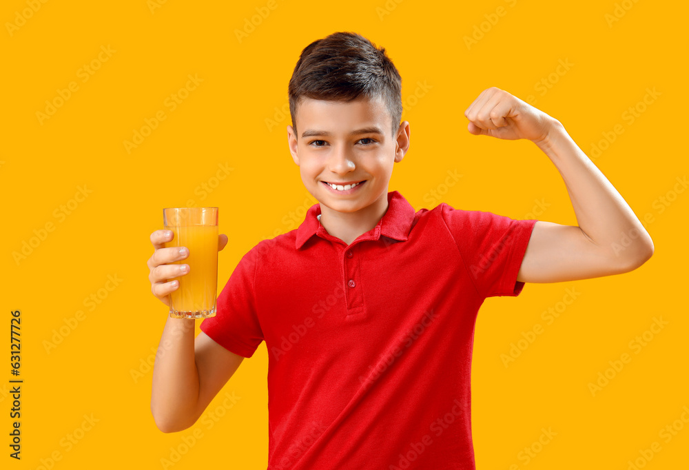 Little boy with glass of orange juice showing muscles on color background