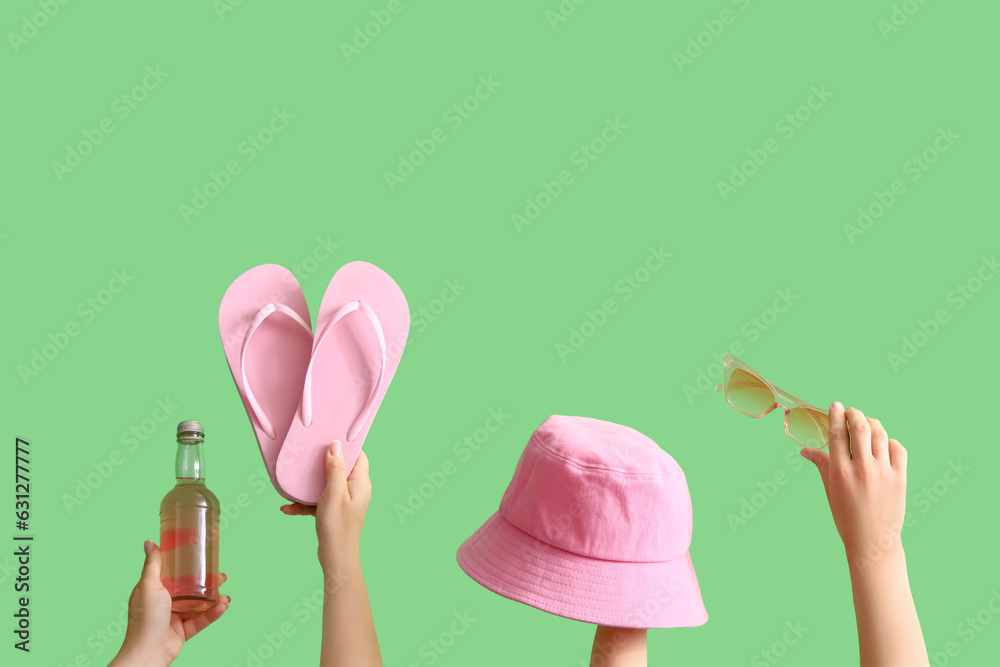 Many hands with beach accessories and bottle of cocktail on green background