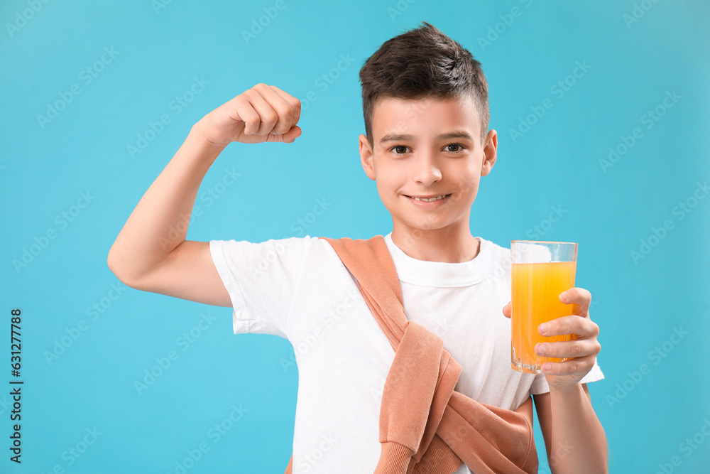 Little boy with glass of orange juice showing muscles on blue background