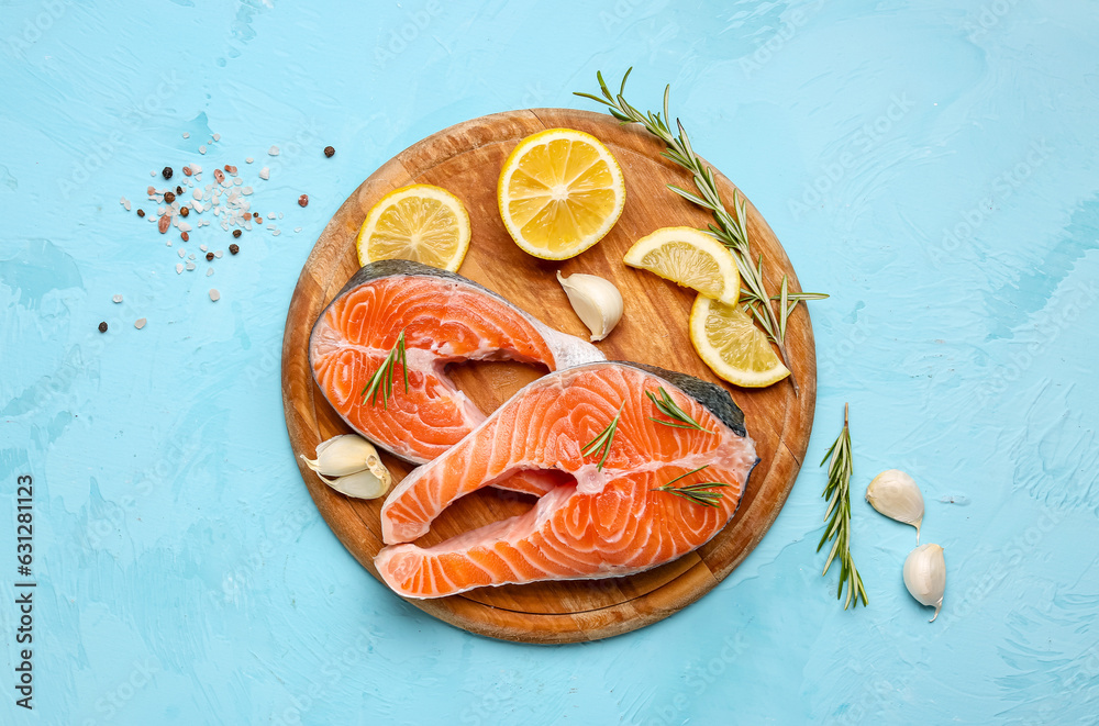 Wooden board with raw salmon steaks and different spices on blue background