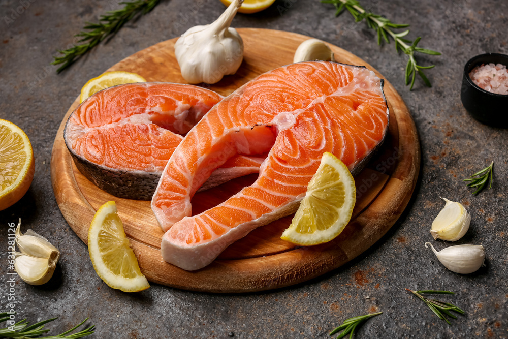 Wooden board with raw salmon steaks and different spices on dark background