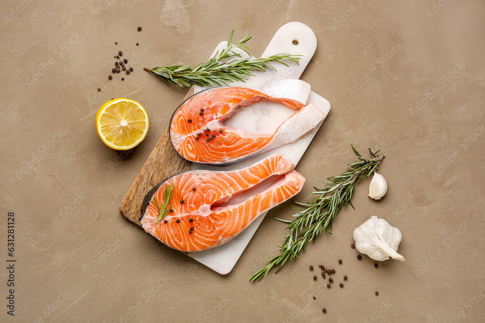 Board with raw salmon steaks and different spices on brown background