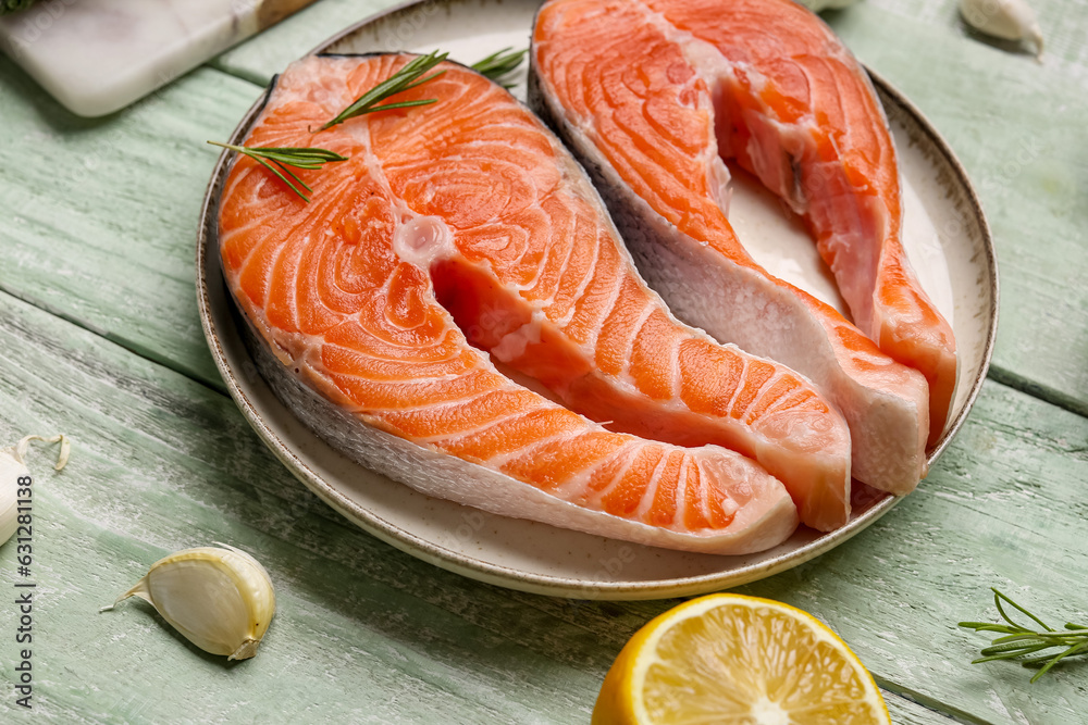 Plate with raw salmon steaks and different spices on green wooden background