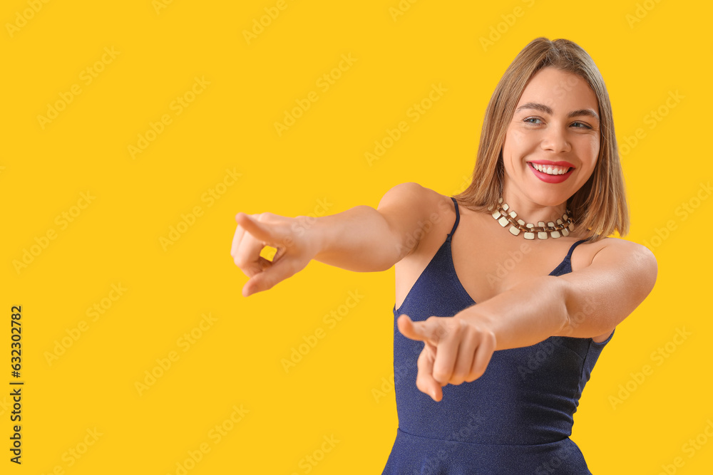 Young woman with necklace pointing at something on yellow background