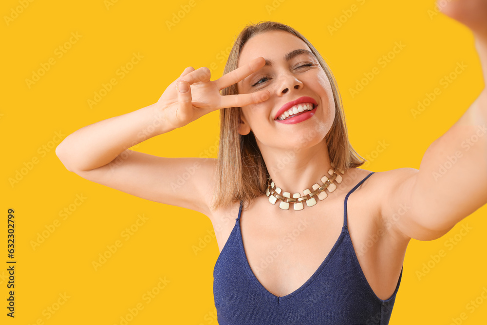 Young woman with necklace showing victory gesture on yellow background, closeup