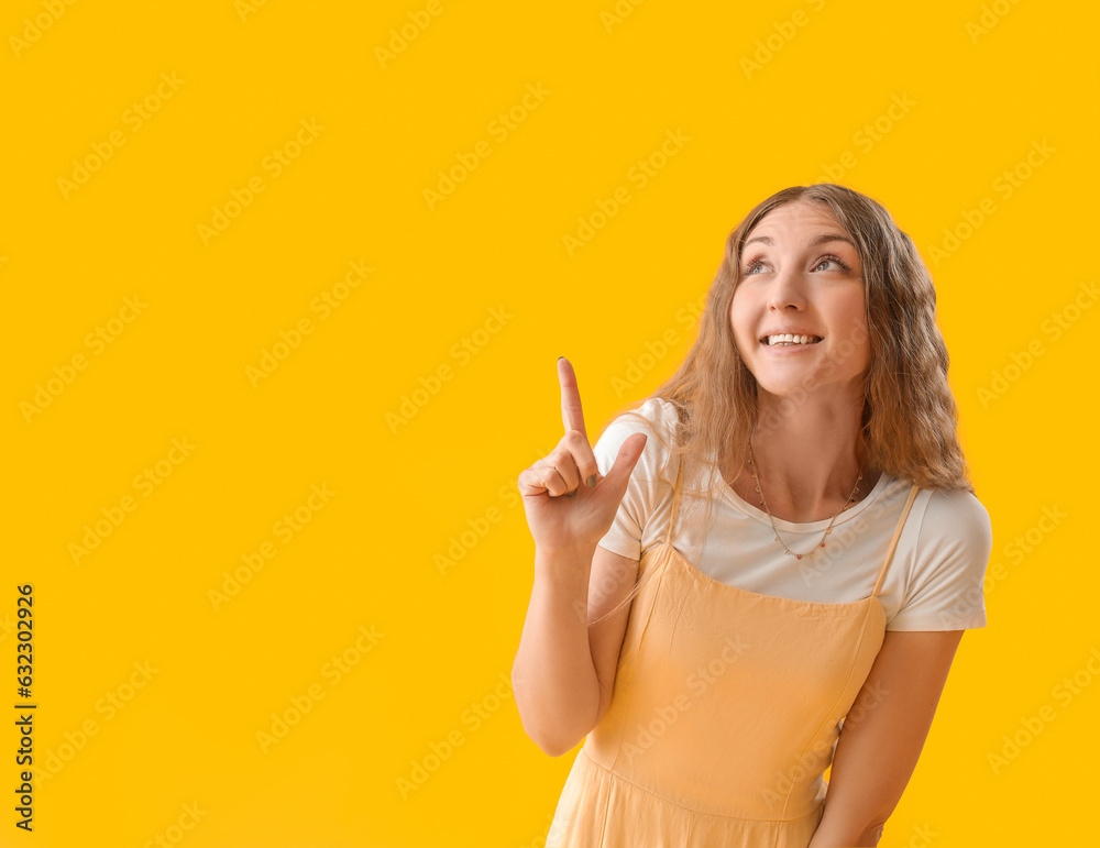 Beautiful young woman pointing at something on yellow background