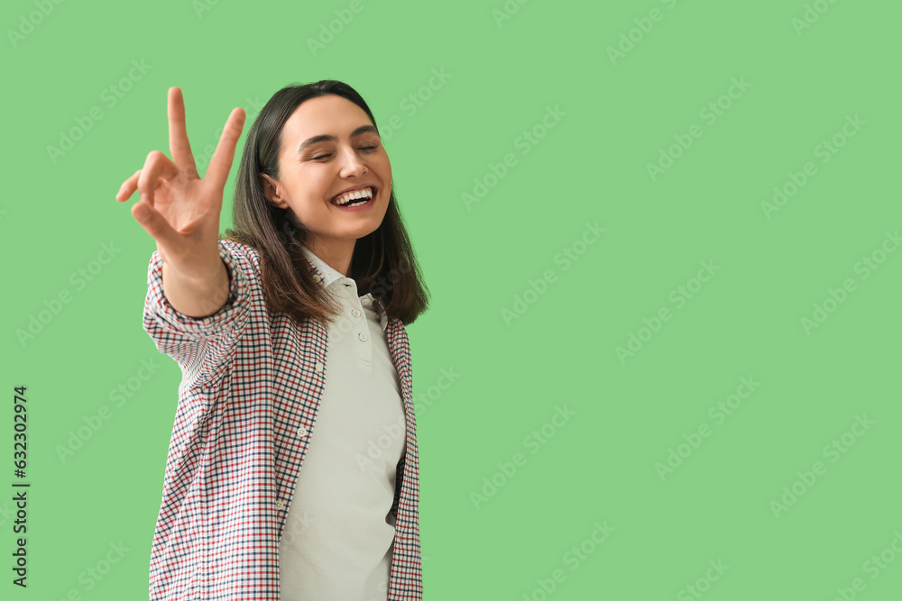 Happy young woman showing victory gesture on green background