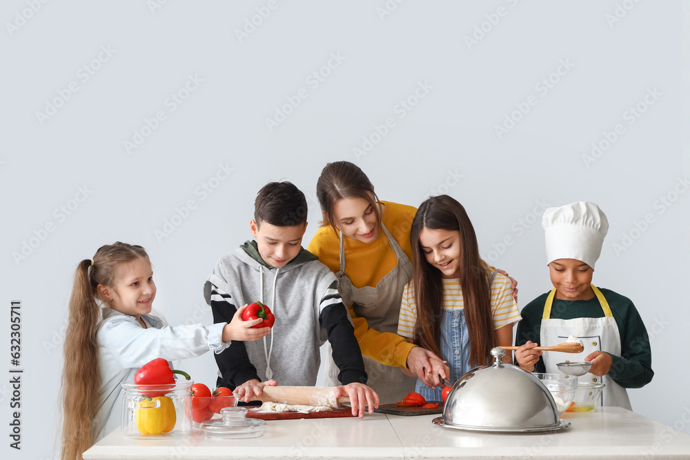 Female chef with group of little children during cooking class on light background