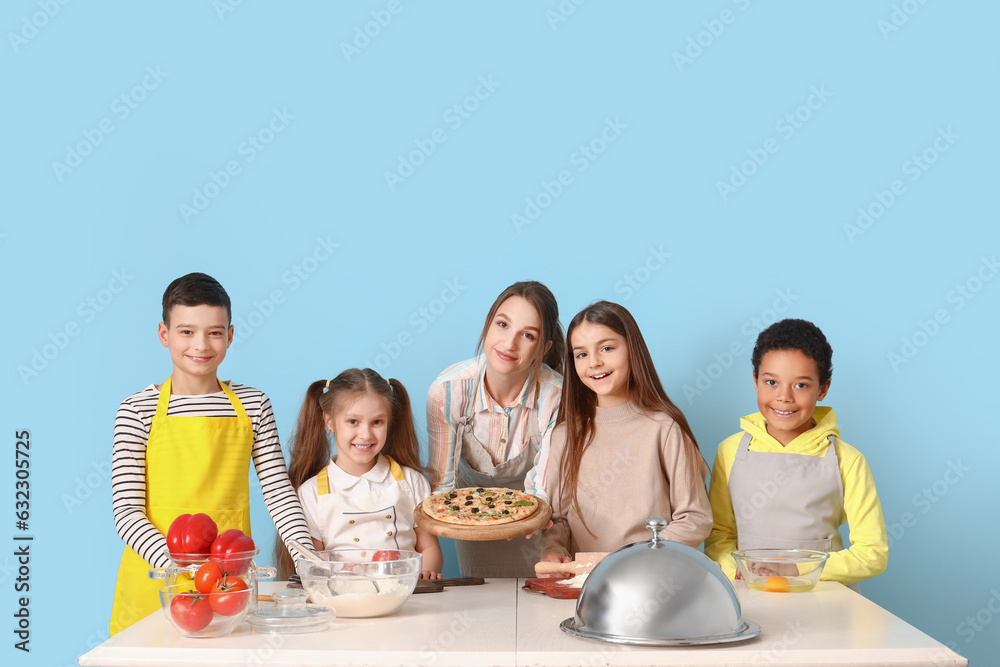 Female chef with prepared pizza and group of little children during cooking class on blue background