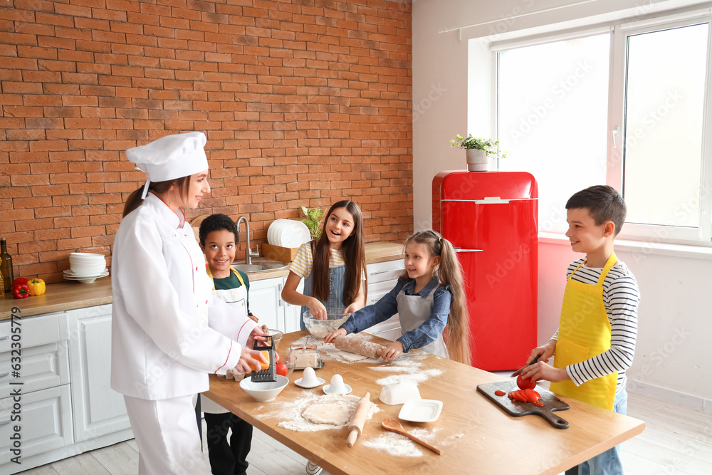 Female chef with group of little children preparing pizza during cooking class in kitchen