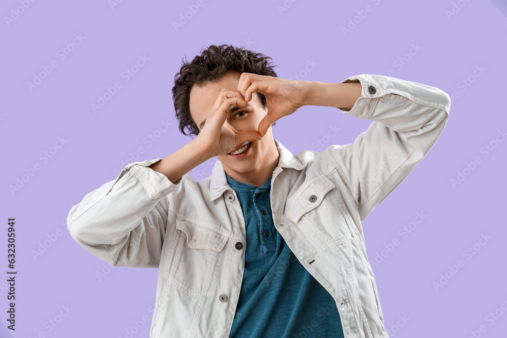 Young man making heart with his hands on lilac background