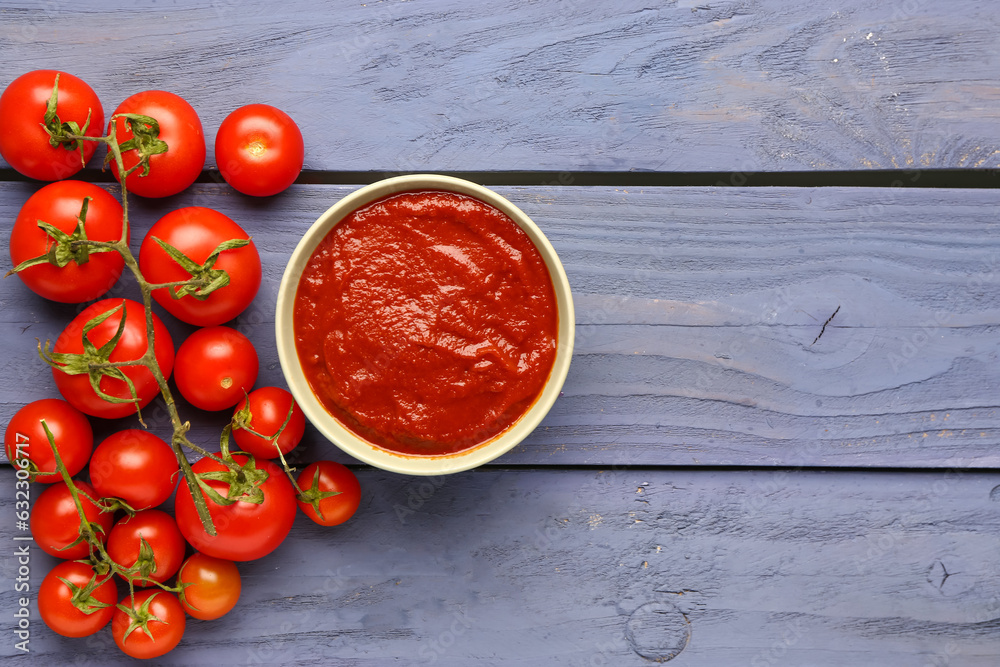 Bowl with tasty tomato paste and fresh vegetables on blue wooden background