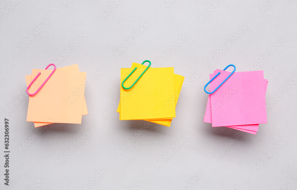 Beige, yellow and pink sticky notes with paper clips on grey background