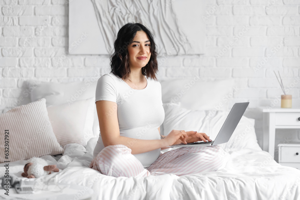 Young pregnant woman working with laptop in bedroom