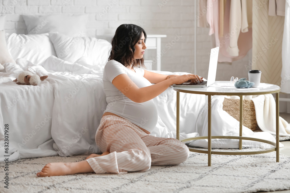 Young pregnant woman working with laptop in bedroom