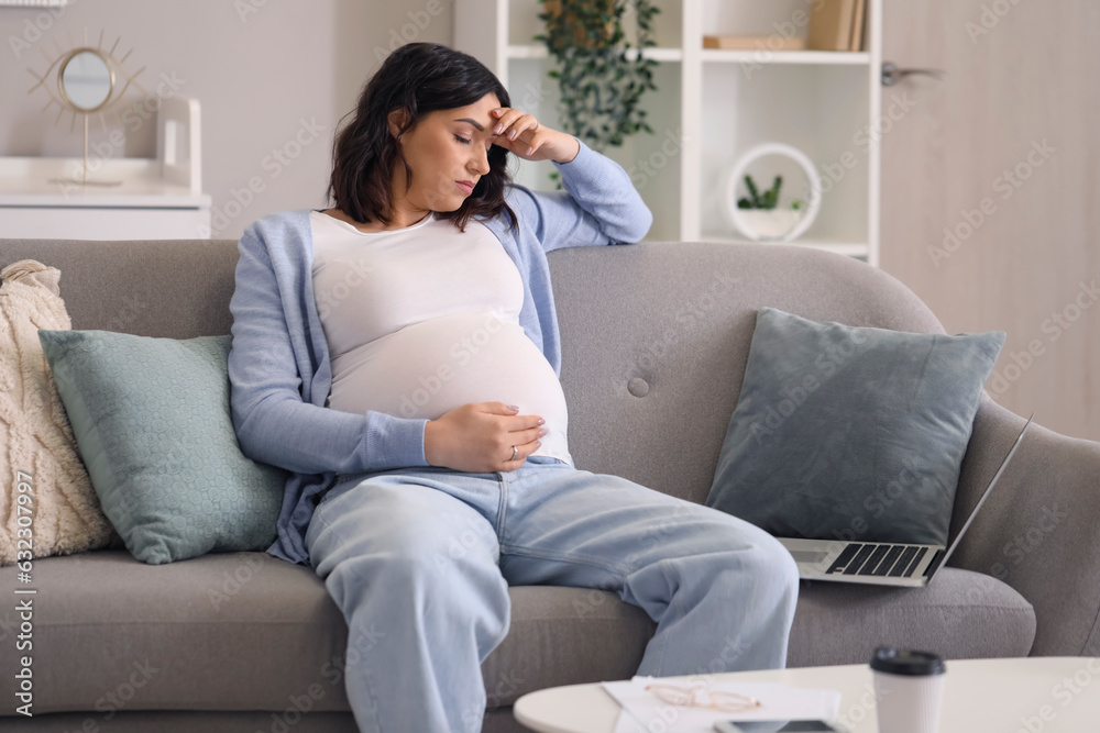 Tired young pregnant woman working with laptop at home