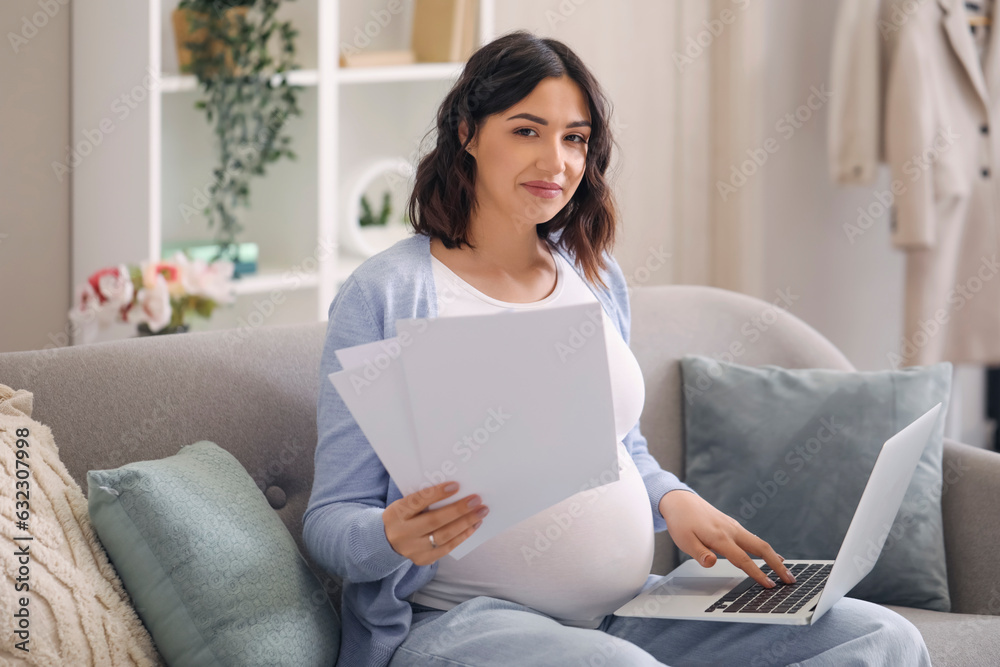 Young pregnant woman working with documents and laptop at home