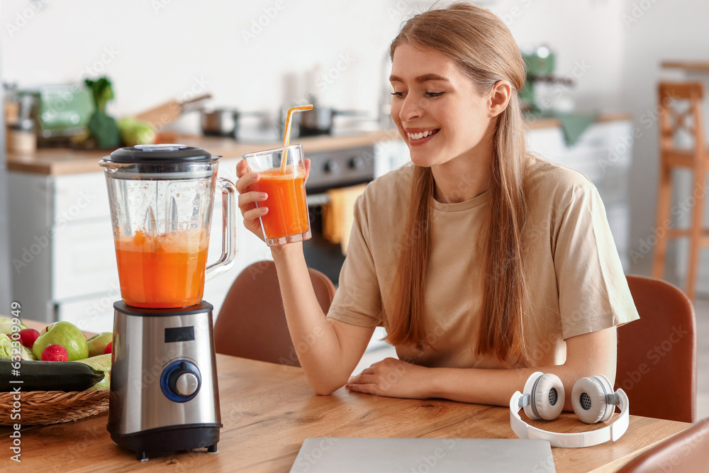 Young woman with healthy smoothie and blender in kitchen