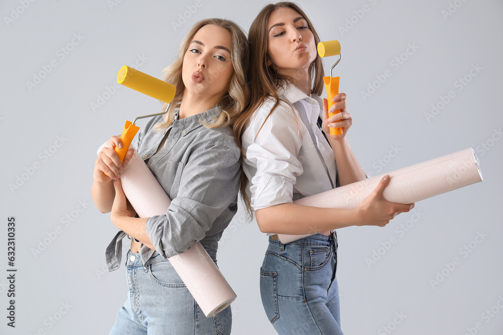 Young women with wallpapers and rollers on grey background