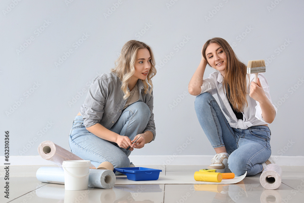 Young women gluing wallpaper rolls near grey wall