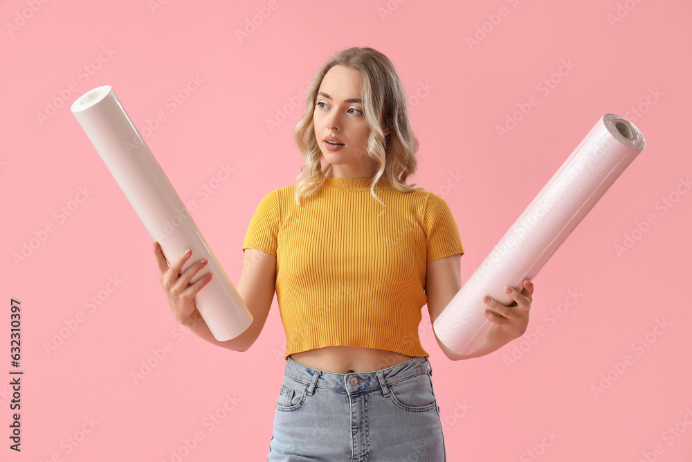 Young woman with wallpaper rolls on pink background