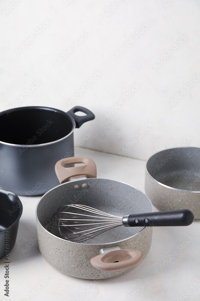 Set of cooking pots and whisk on light background