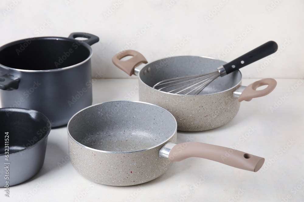 Set of cooking pots and whisk on light background, closeup