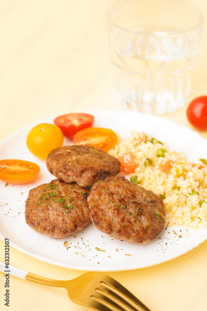 Cutlets with bulgur, boiled vegetables and tomatoes on light yellow table in kitchen