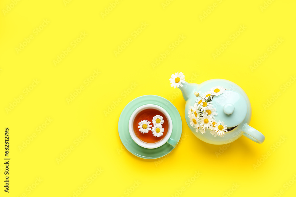 Teapot with cup of natural chamomile tea and flowers on yellow background