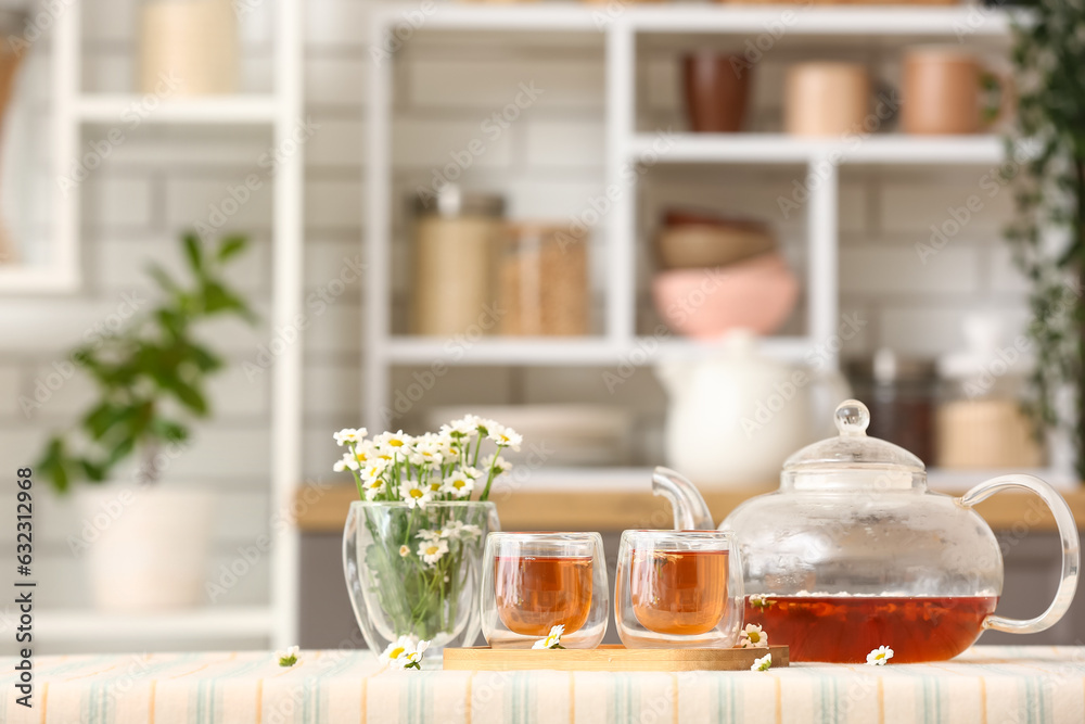 Wooden tray with teapot, cups of natural chamomile tea and flowers on table in kitchen