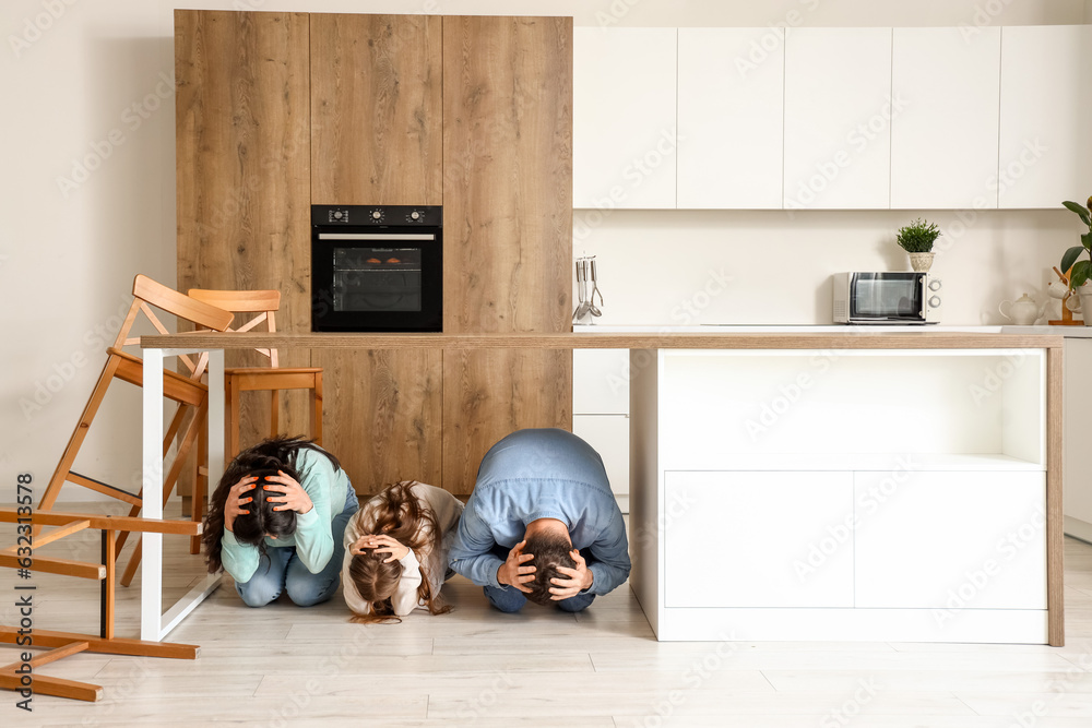 Scared family hiding under dining table during earthquake in kitchen