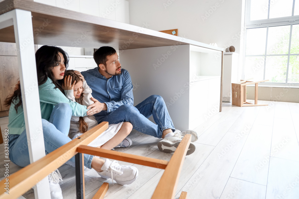 Scared family hiding under dining table during earthquake in kitchen