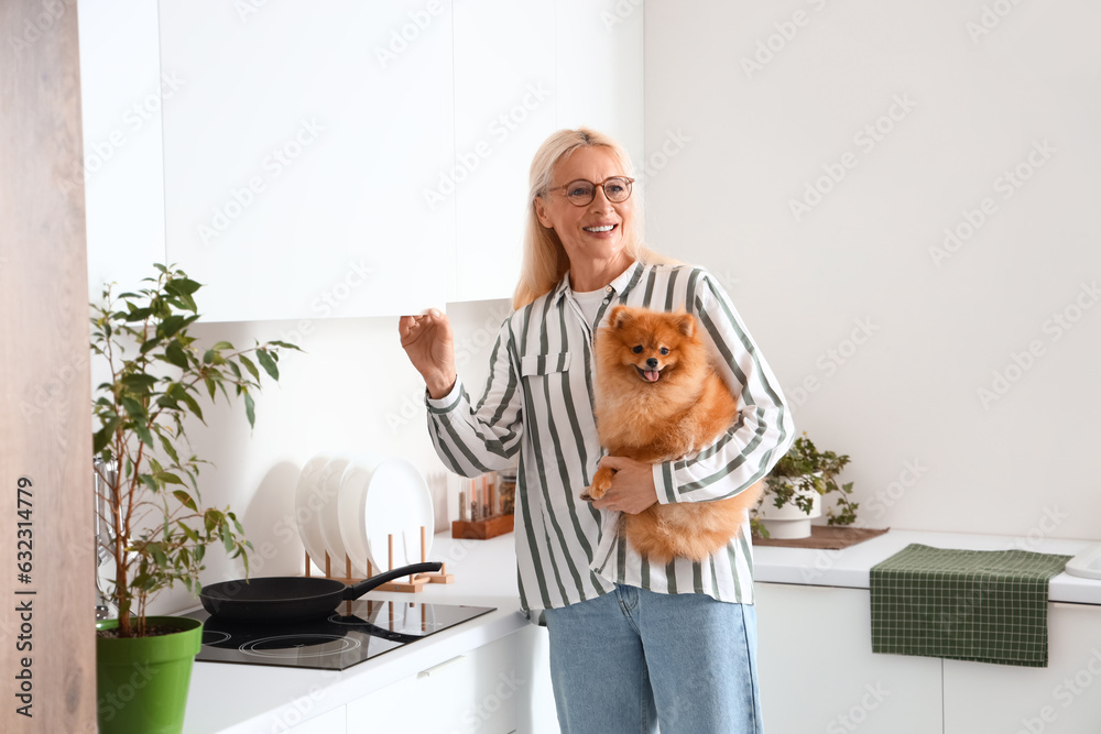 Mature woman with Pomeranian dog opening drawer in kitchen