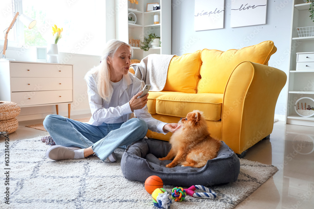 Mature woman with mobile phone taking picture of her Pomeranian dog at home