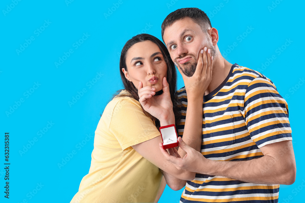 Happy young couple with engagement ring on blue background