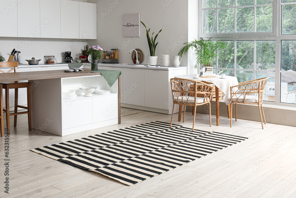 Interior of modern kitchen with white counters, island and dining table near big window