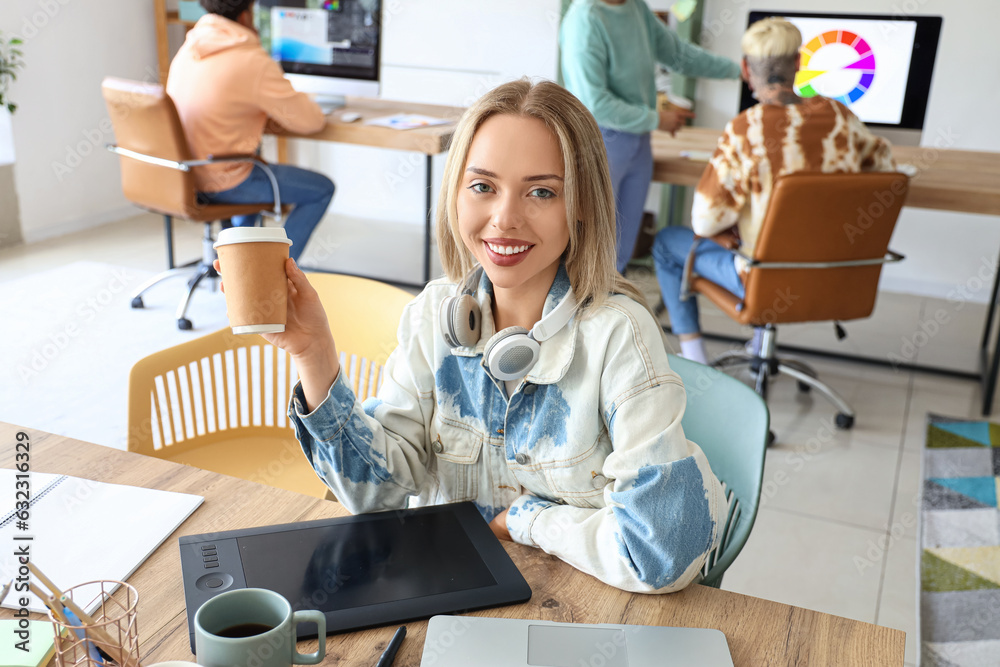 Female graphic designer with cup of coffee working at table in office