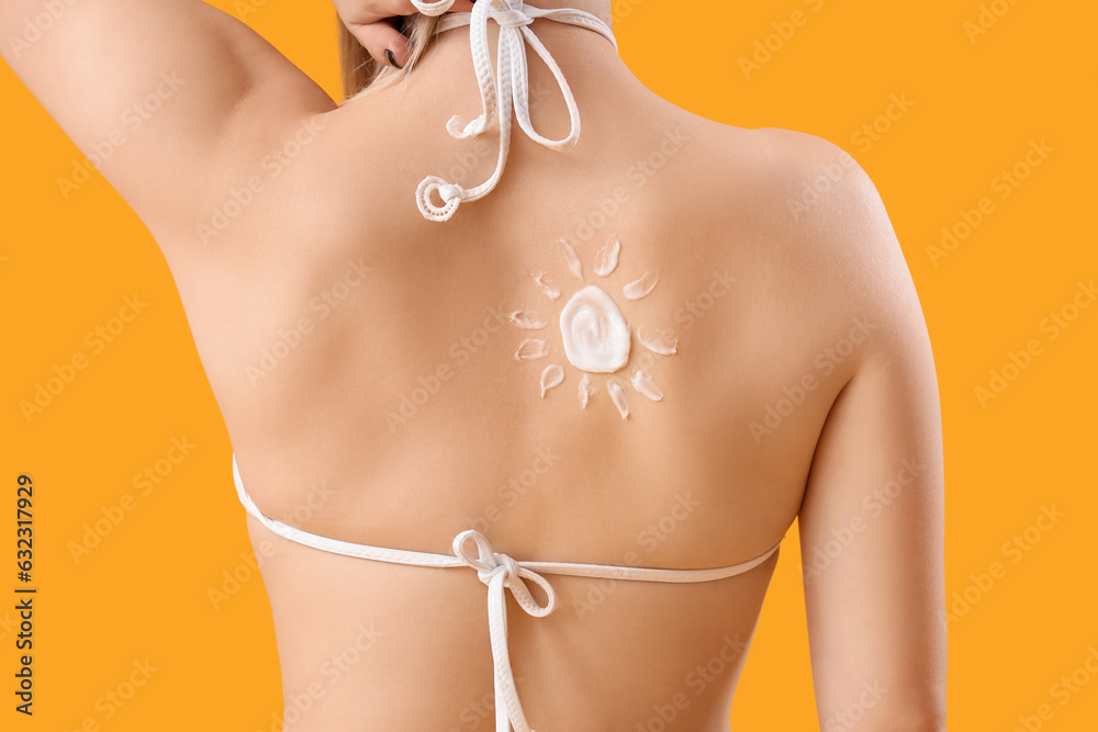 Young woman with sun made of sunscreen cream on her back against yellow background