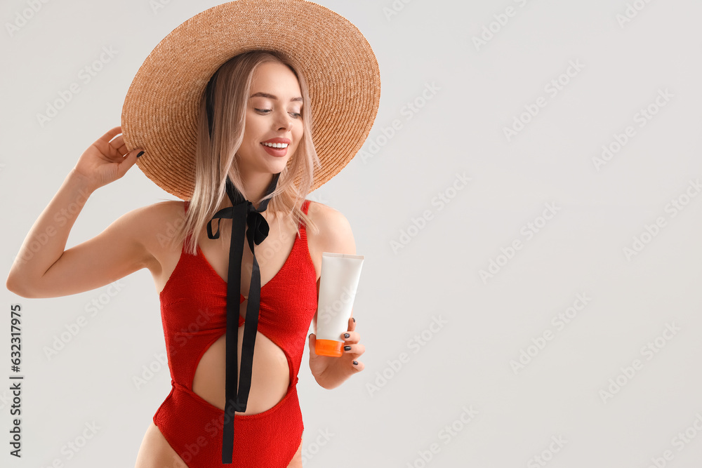 Young woman with sunscreen cream on light background