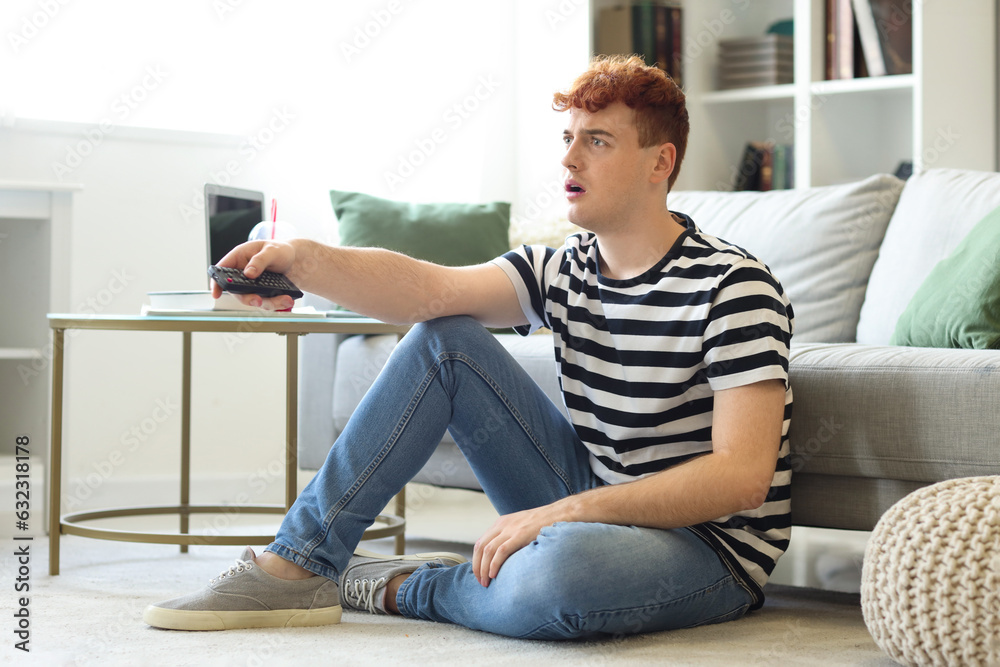 Shocked young redhead man watching TV at home