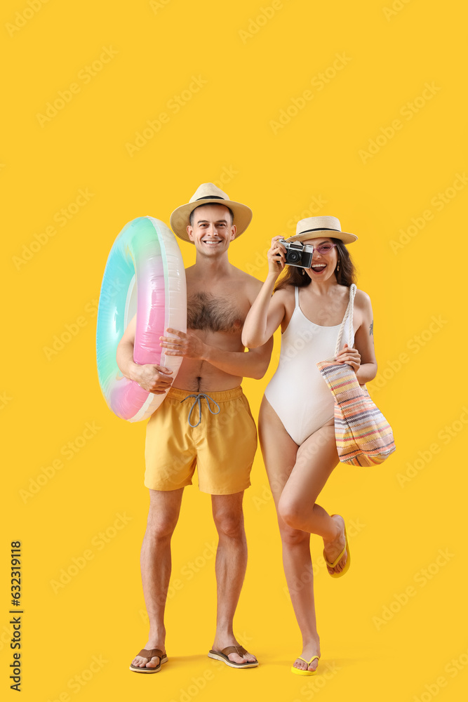 Young couple with inflatable ring and photo camera on yellow background