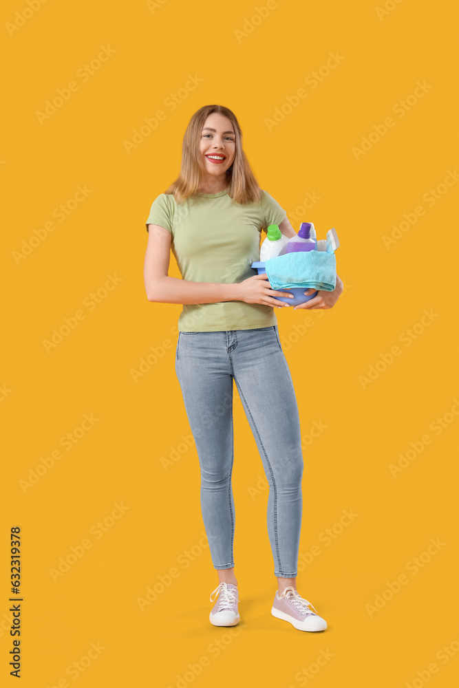 Young woman with cleaning supplies on orange background