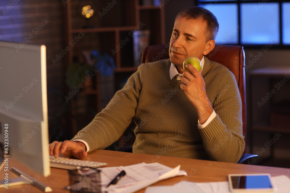 Mature man with apple working in office at night