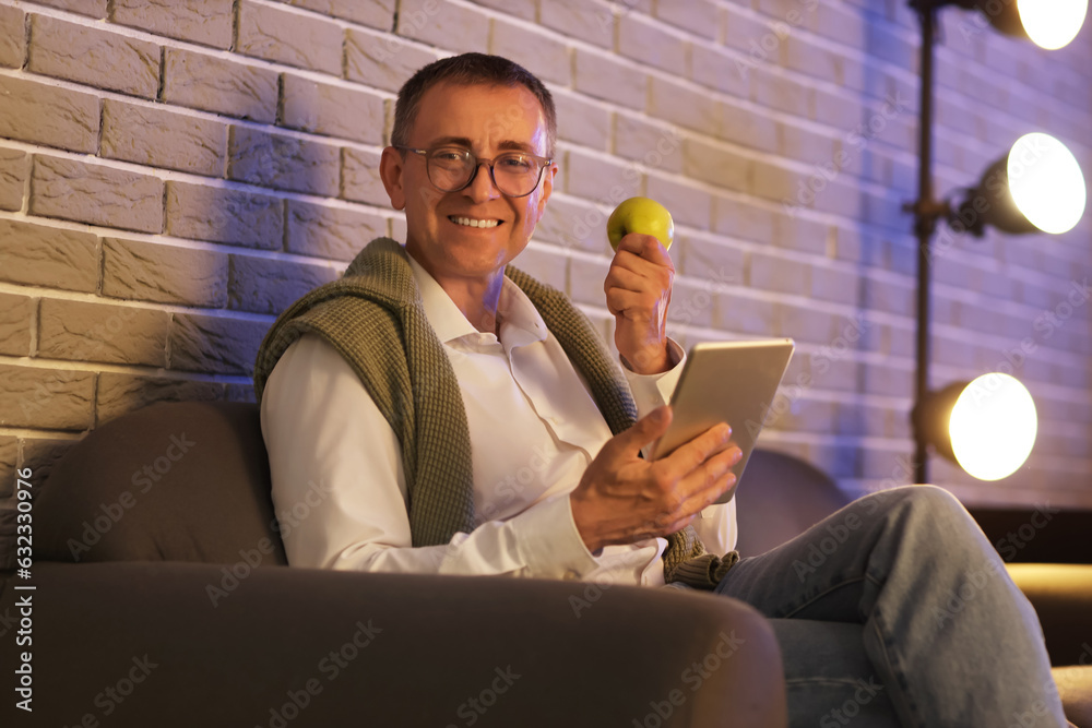 Mature man with tablet computer and apple in office at night