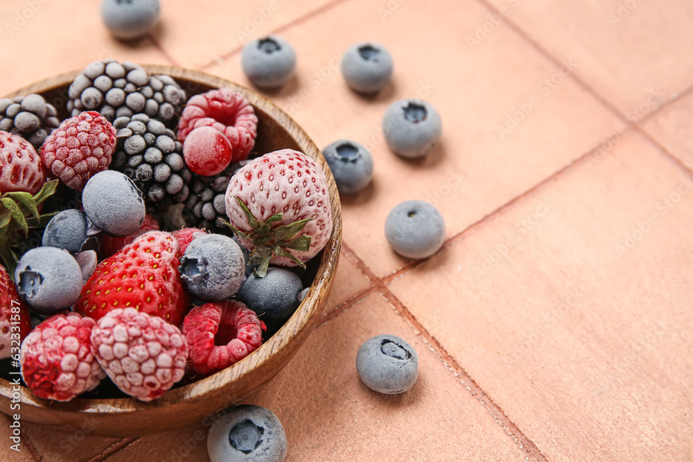 Bowl of different frozen berries on color tile background