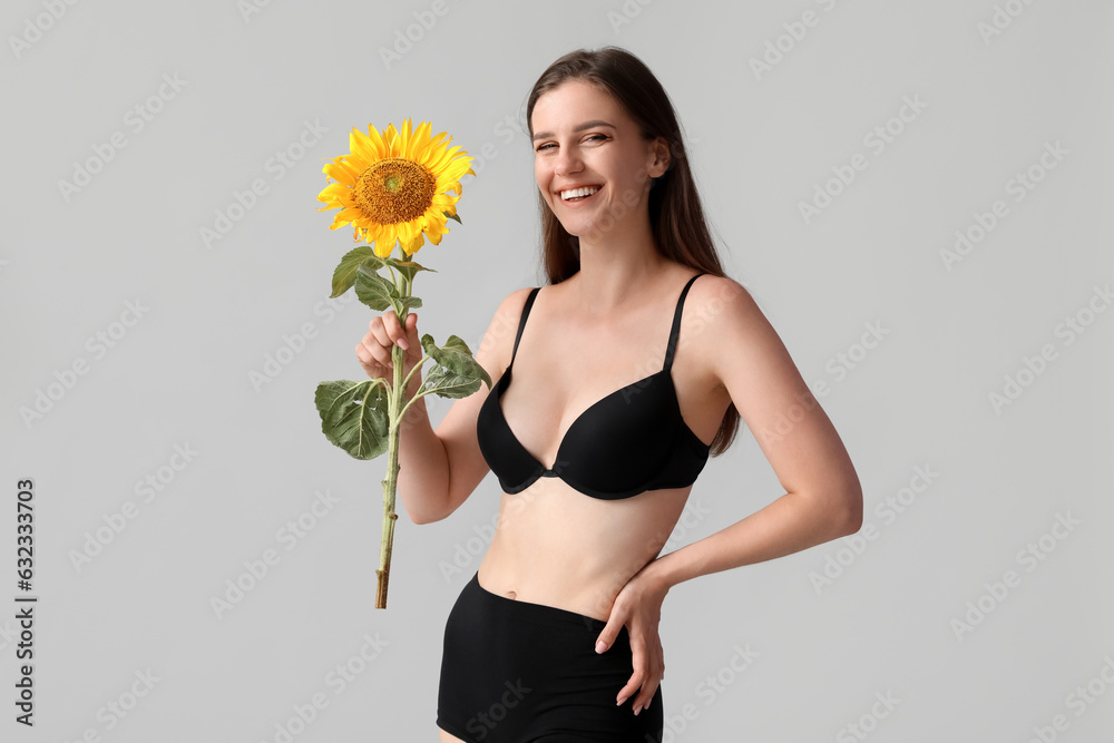 Young happy woman in underwear with beautiful sunflower on grey background